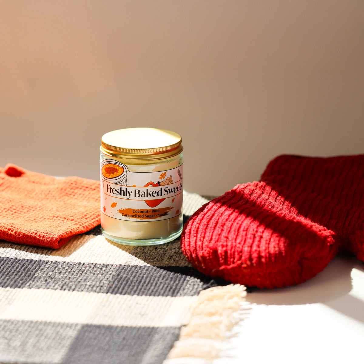 Jar of freshly baked sweets candle with red mitten and a kitchen towel on a checkered cloth.