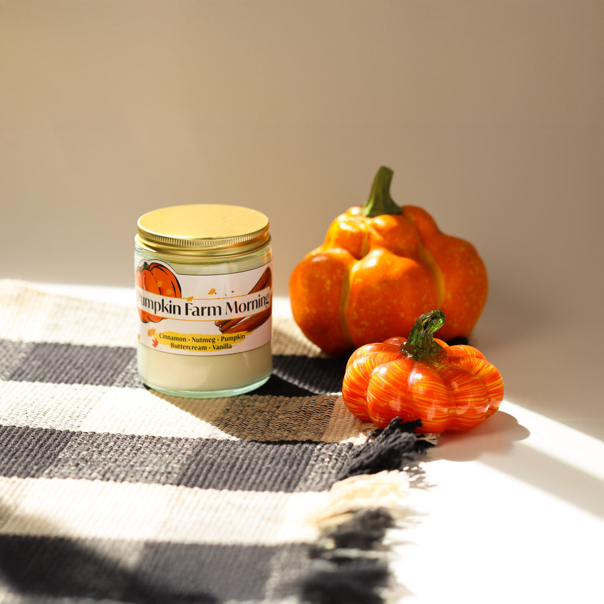 Jar of pumpkin farm morning candle with decorative pumpkins on a checkered cloth