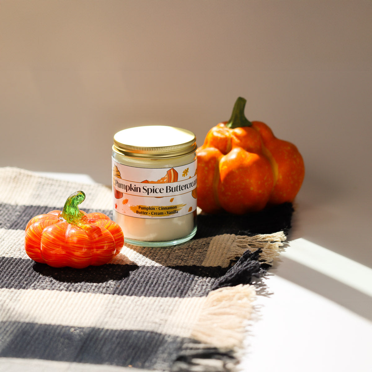 Jar of pumpkin spice buttercream candle with decorative pumpkins on a checkered cloth.