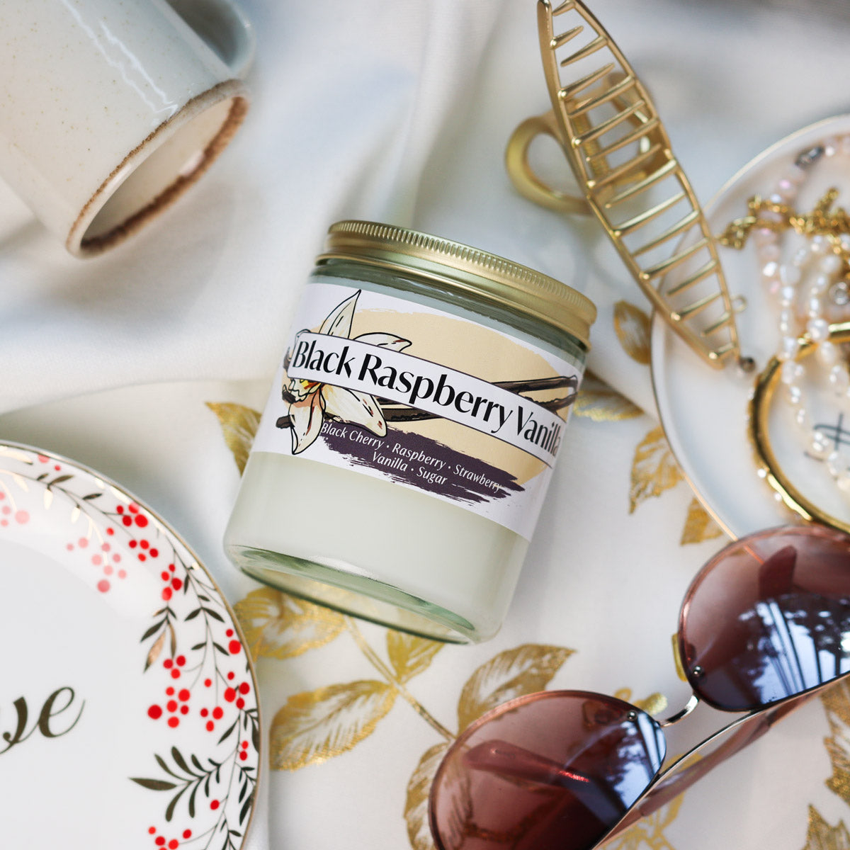 Jar of Black Raspberry Vanilla Candle on a decorative tablecloth with accessories around it
