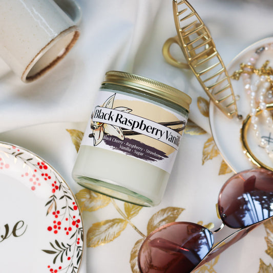 Jar of Black Raspberry Vanilla Candle on a decorative tablecloth with accessories around it