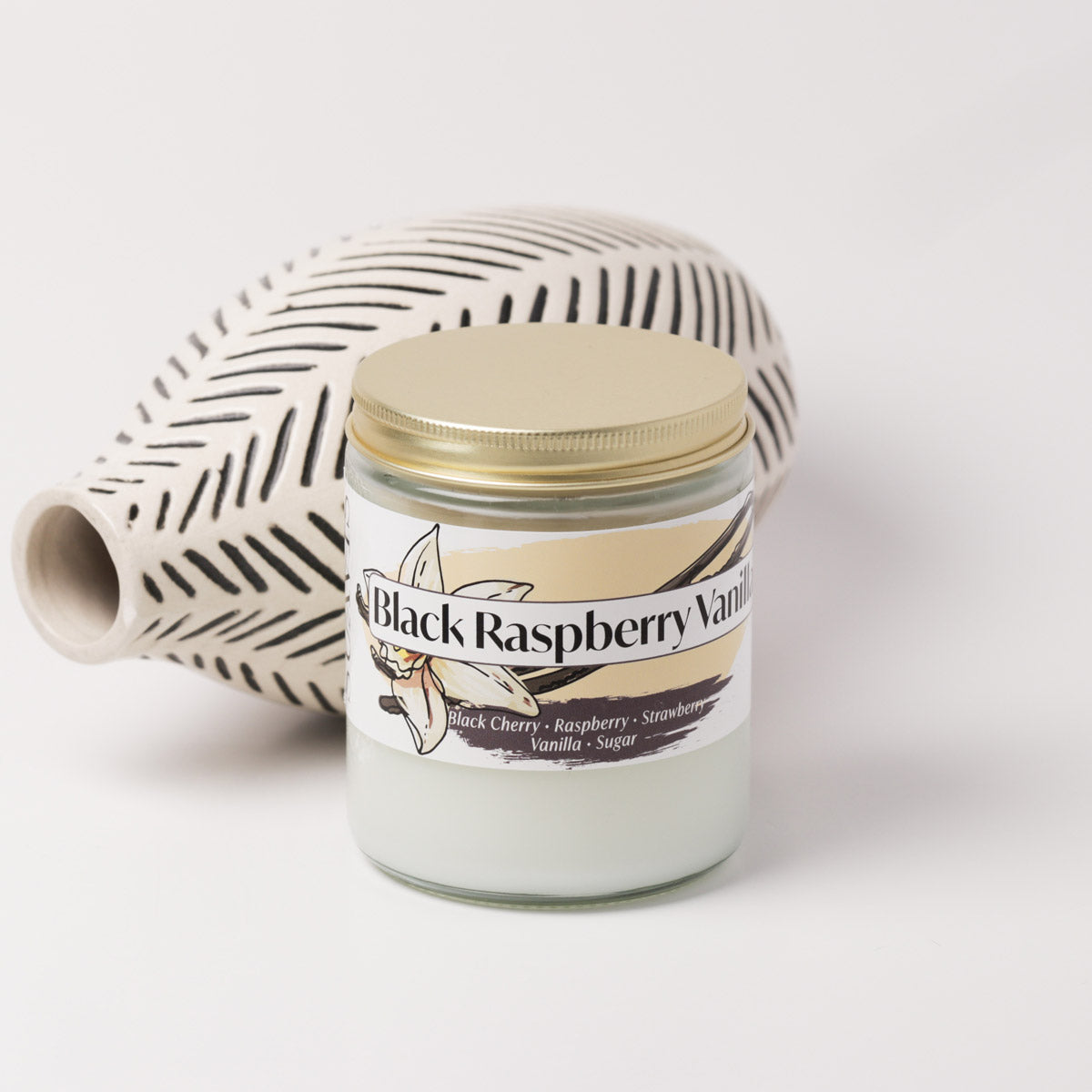Black raspberry vanilla candle on a white background next to a vase
