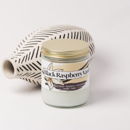 Black raspberry vanilla candle on a white background next to a vase