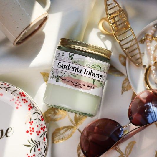 Jar of Gardenia Tuberose Candle on a decorative tablecloth with accessories around it