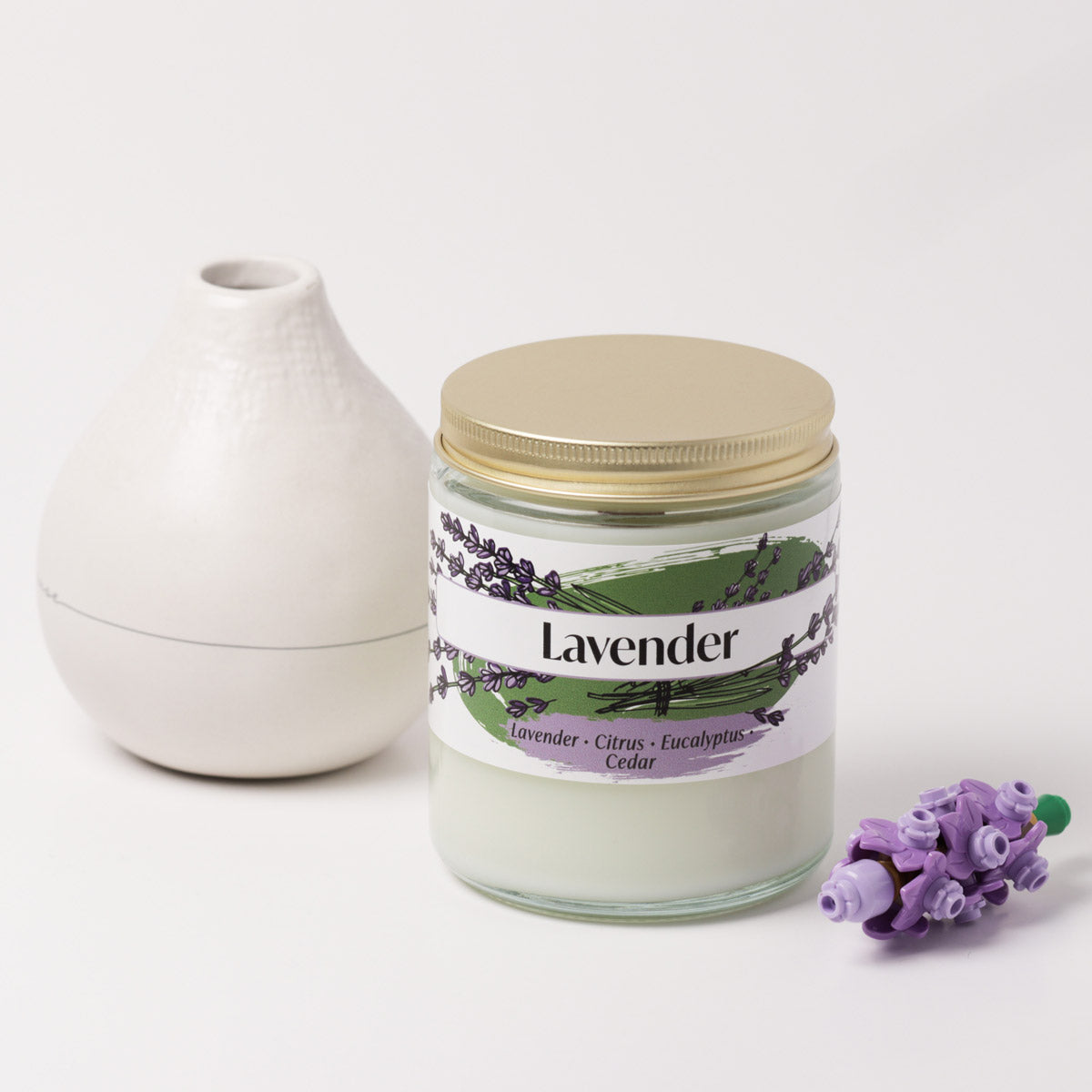 Lavender candle on a white background next to a vase and plastic flower