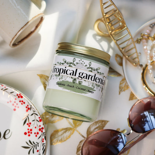Jar of Tropical Gardenia Candle on a decorative tablecloth with accessories around it